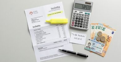 Immagine di una scrivania bianca con un documento di fattura, un evidenziatore, una calcolatrice, banconote e un documento d'identità.