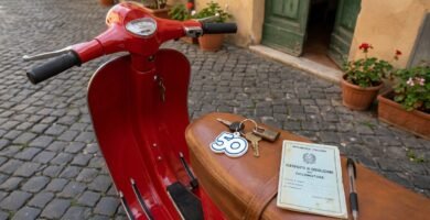 Immagine ravvicinata di uno scooter rosso accanto alle chiavi e al libretto di circolazione sul sedile.