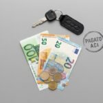 Immagine di una chiave, monete e banconote in euro su una scrivania color piombo.