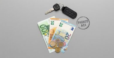 Immagine di una chiave, monete e banconote in euro su una scrivania color piombo.