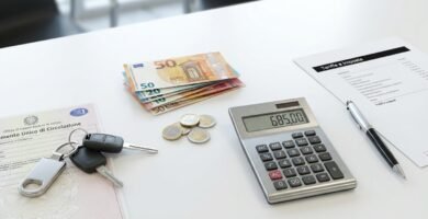 Immagine di una calcolatrice, tasti, penne e banconote su una scrivania bianca.